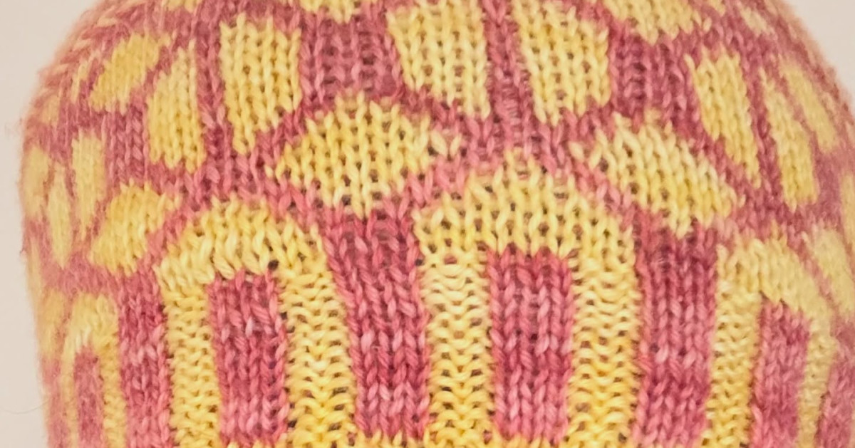 A knitted project in progress with yarn, notes, and a printed pattern on a table.